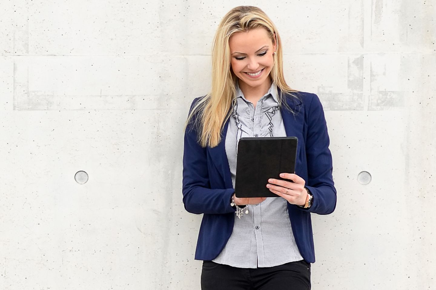 Woman leans on wall and gazes at a tablet smiling. Artistically generated constellation in the form of a padlock.