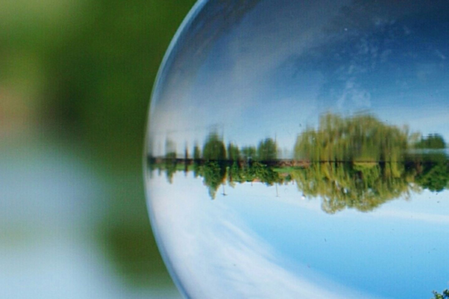 Hand holding glass ball in the sea and green shore visible in the distance.