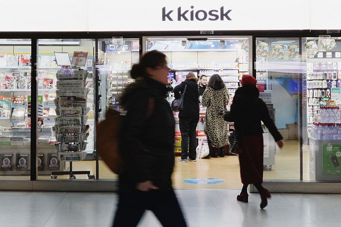 A woman dressed in black passes a kiosk, in which several customers are present.