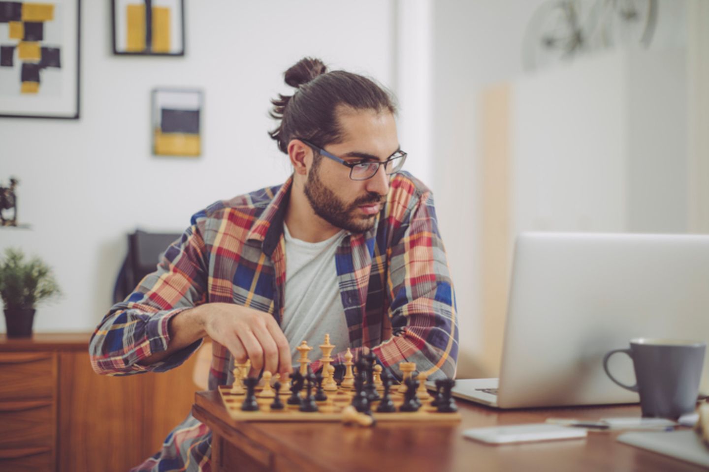 A man playing chest alone and looking on his laptop