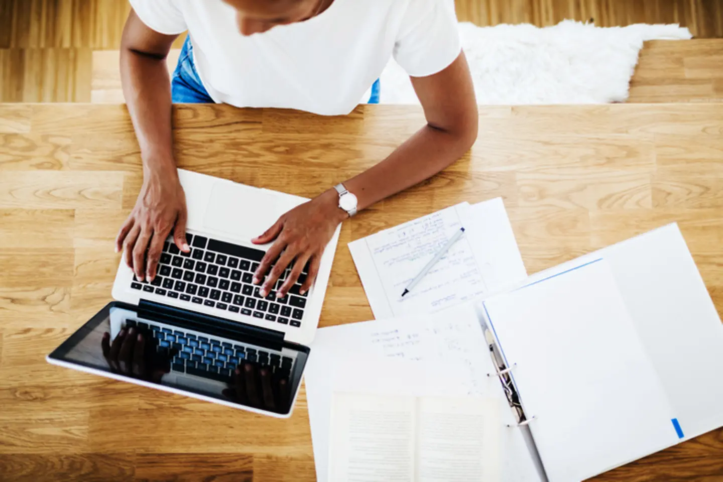 Vogelperspectief van een vrouw die aan een tafel op de laptop werkt.