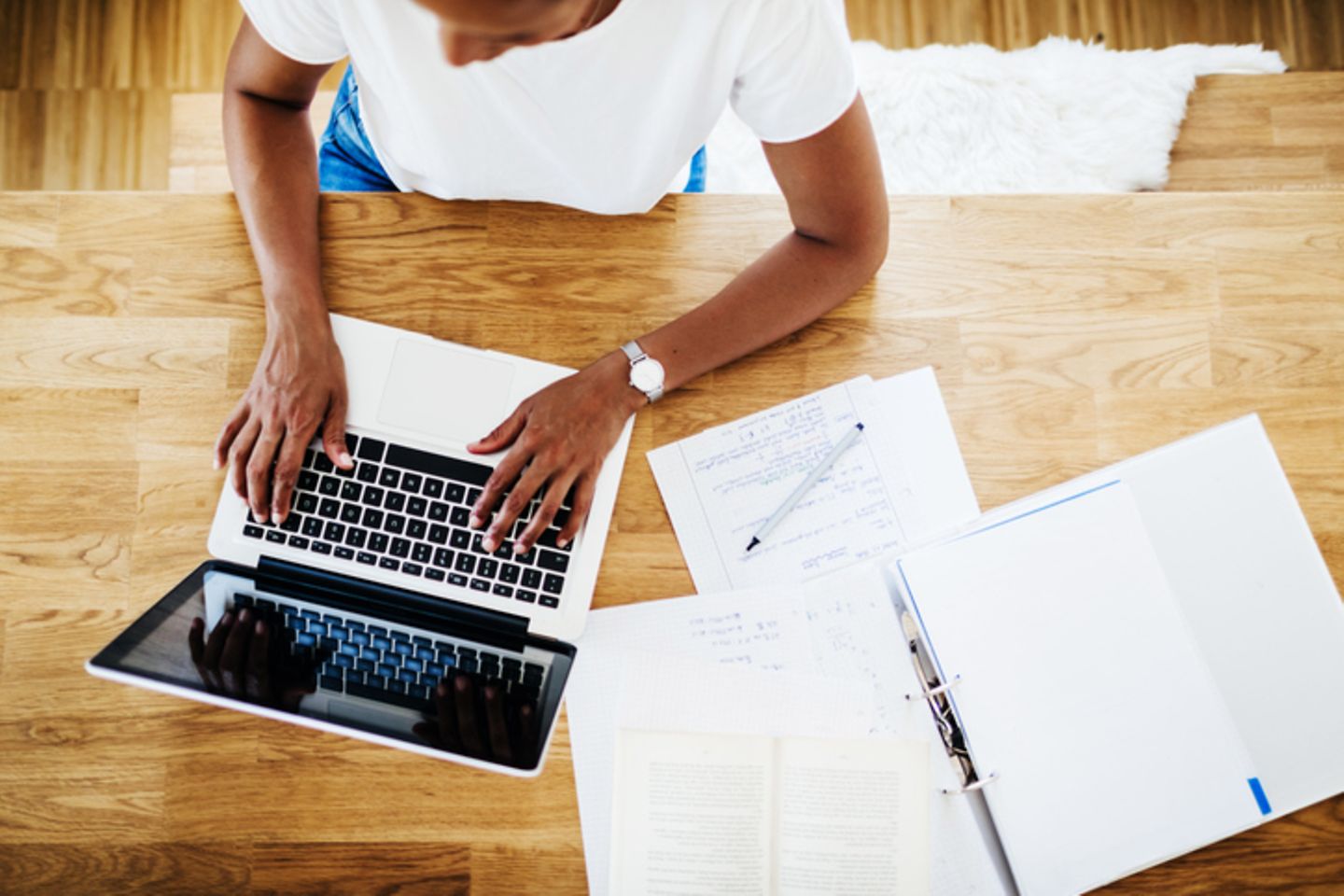 Vogelperspectief van een vrouw die aan een tafel op de laptop werkt.