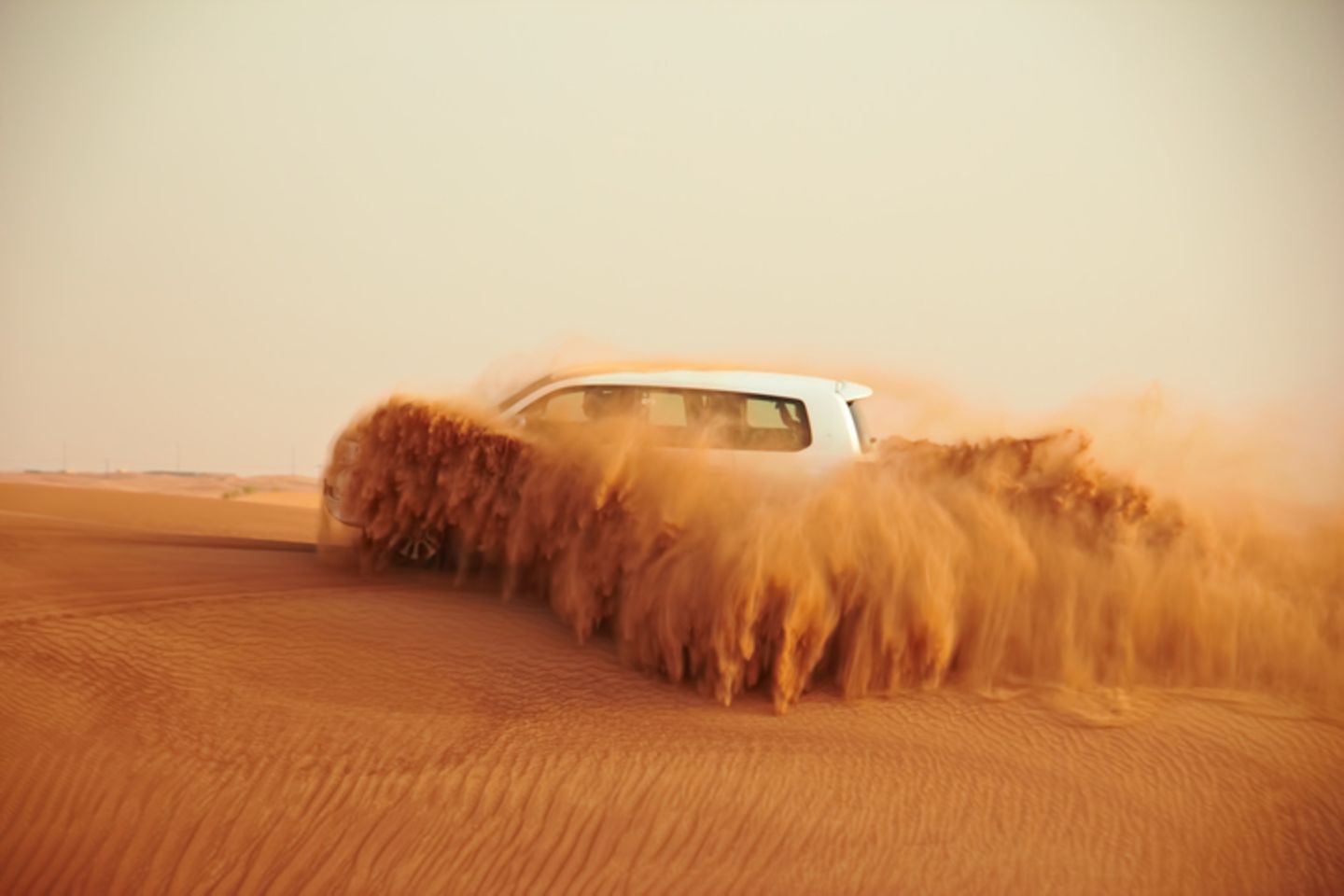 White car driving through ocher-colored, churning desert sand