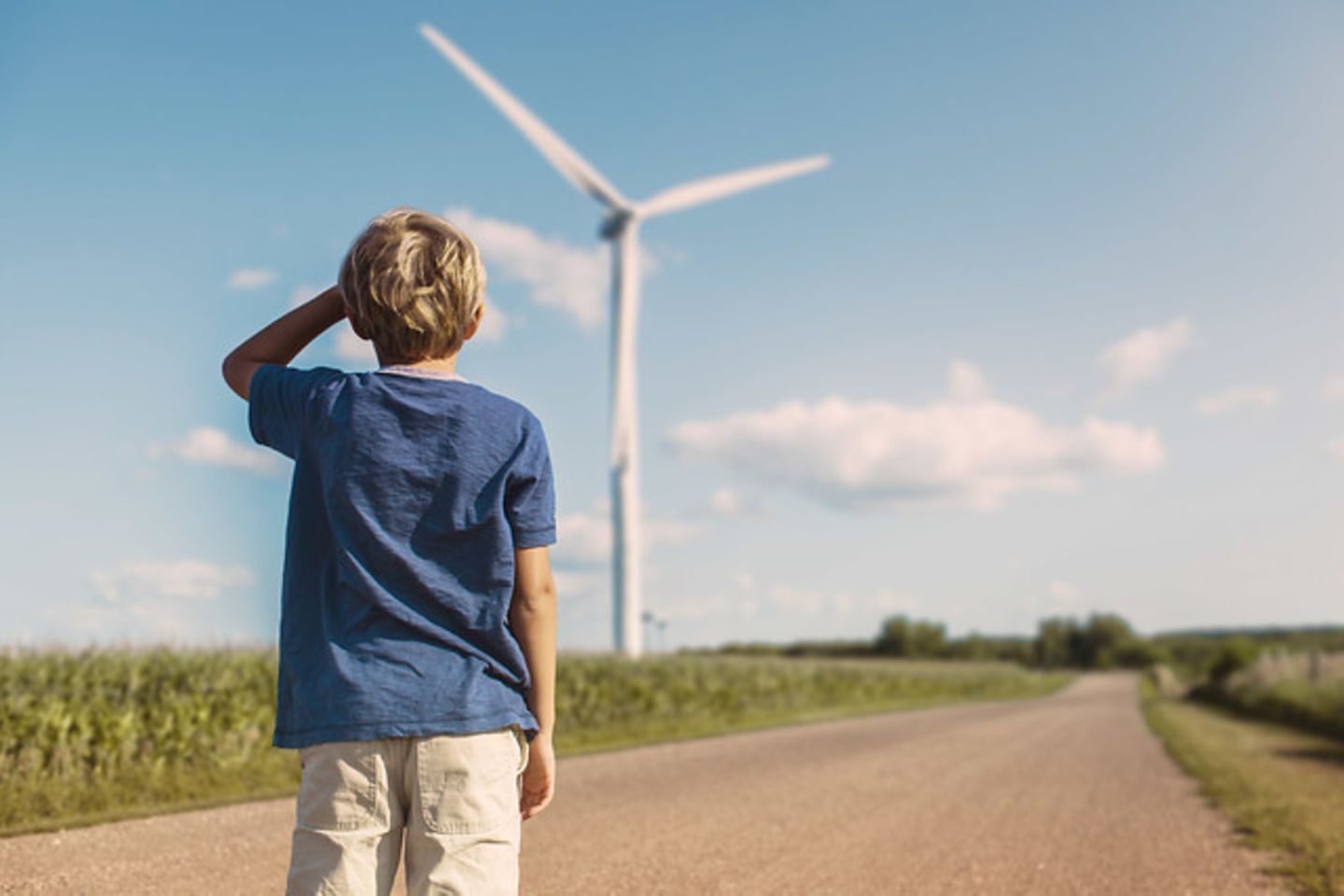 kind kijkt naar windmolen, weg, blauwe lucht