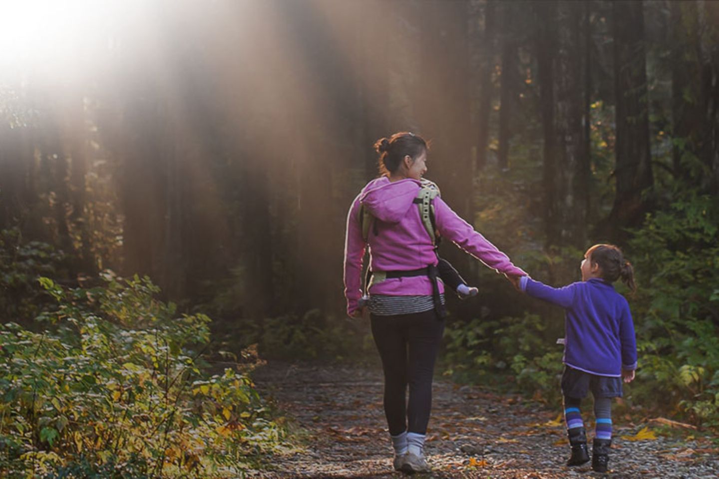 Eine Frau geht mit einem Kind Hand in Hand durch den Wald.