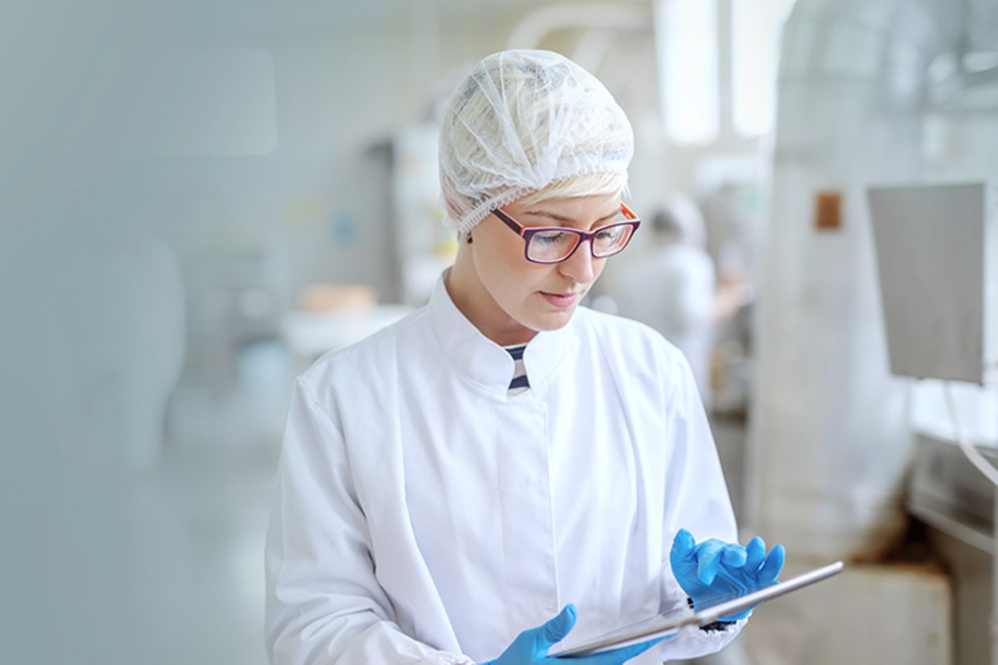 Woman in white work clothes taps on tablet with gloves.