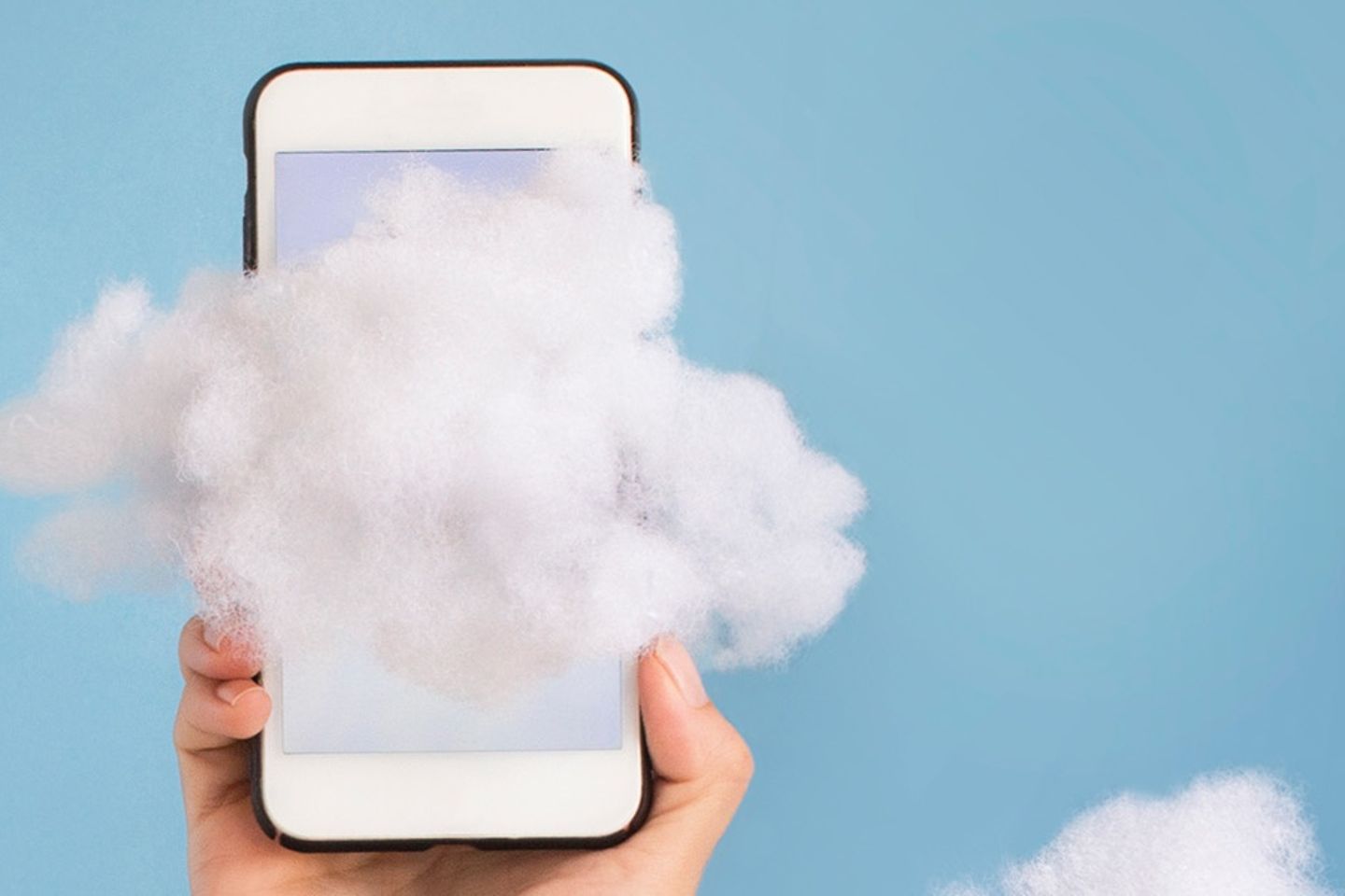 Wolken vor hellblauem Hintergrund in den Arm mit Smartphone ragt.