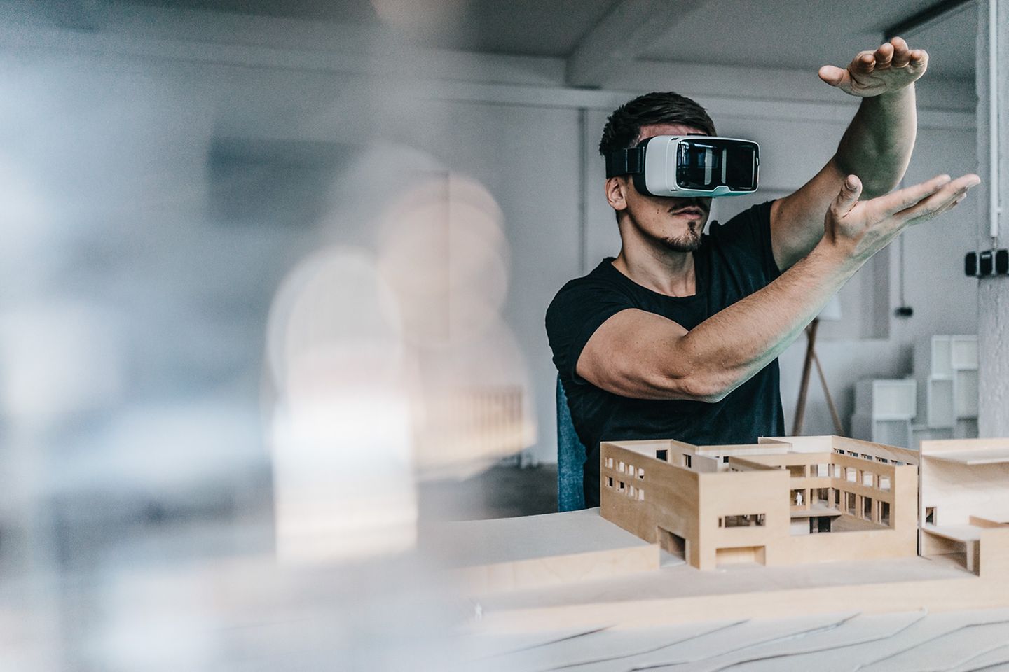 Man met een VR-bril is bezig in een virtuele ruimte. Voor hem staat op de tafel een 3D-model van een fabriek