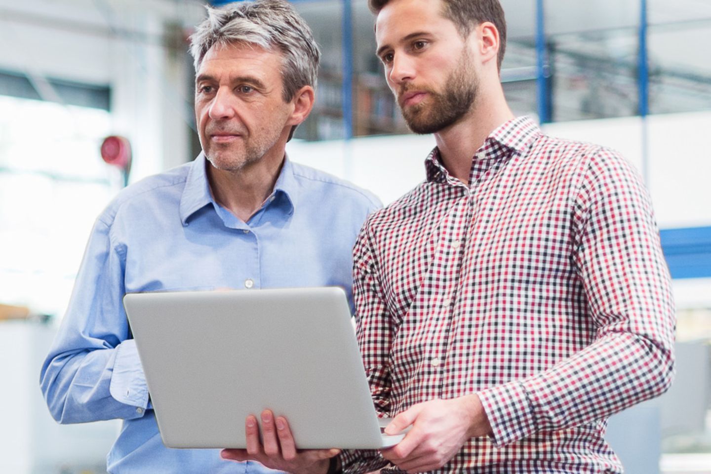 Twee zakenmannen met een laptop in een fabriekshal focussen zich ergens op