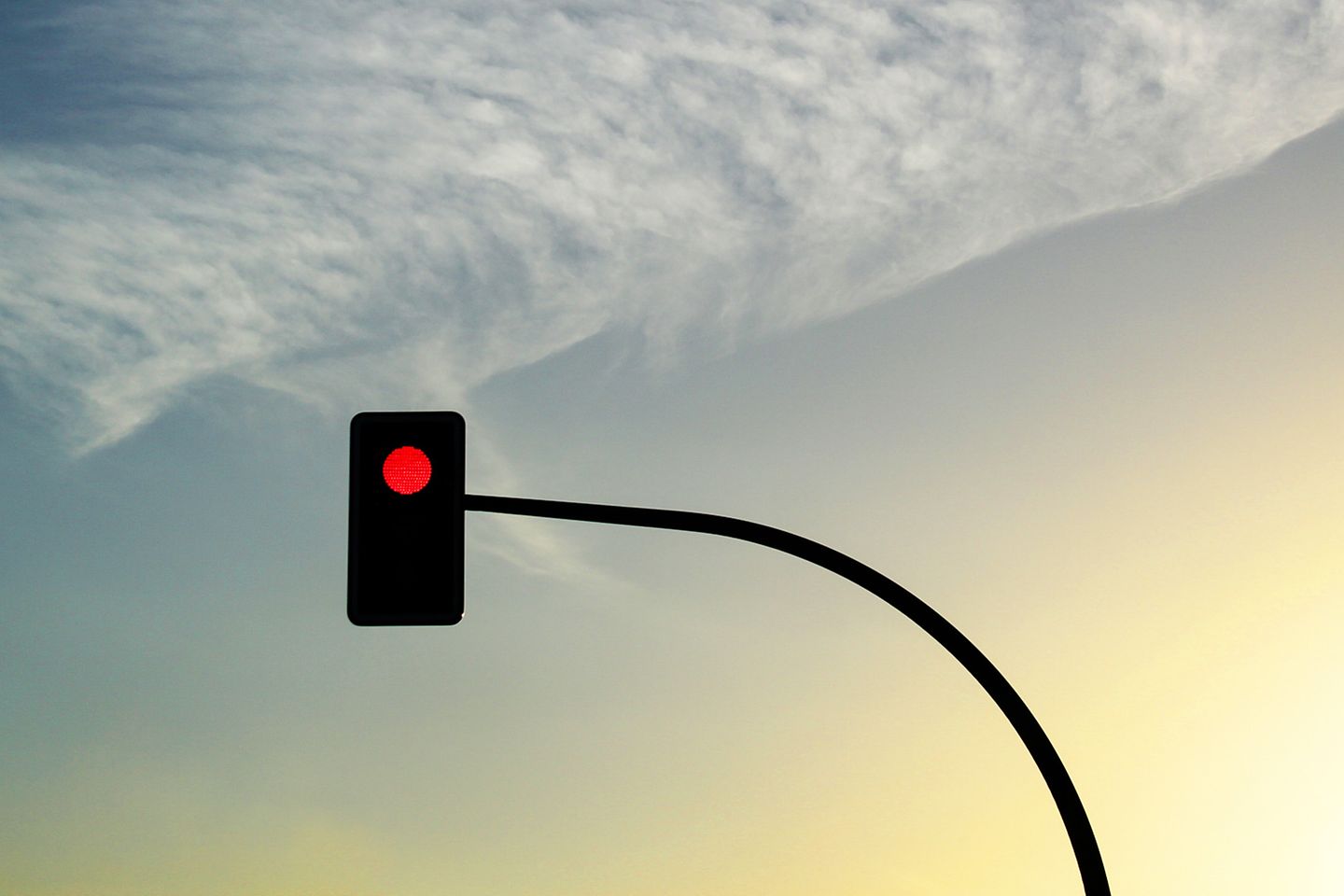 Schilderachtige foto van een wolkenconstellatie bij schemering, met daarvoor een rood stoplicht.