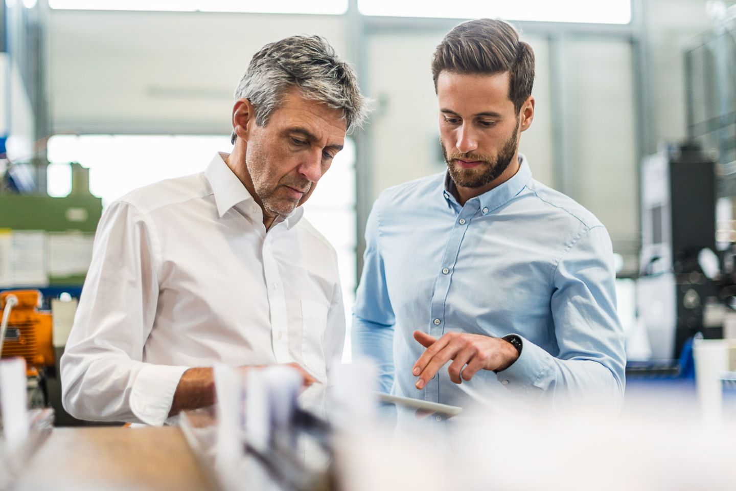 Two casually dressed businessmen standing in a production hall above a tablet