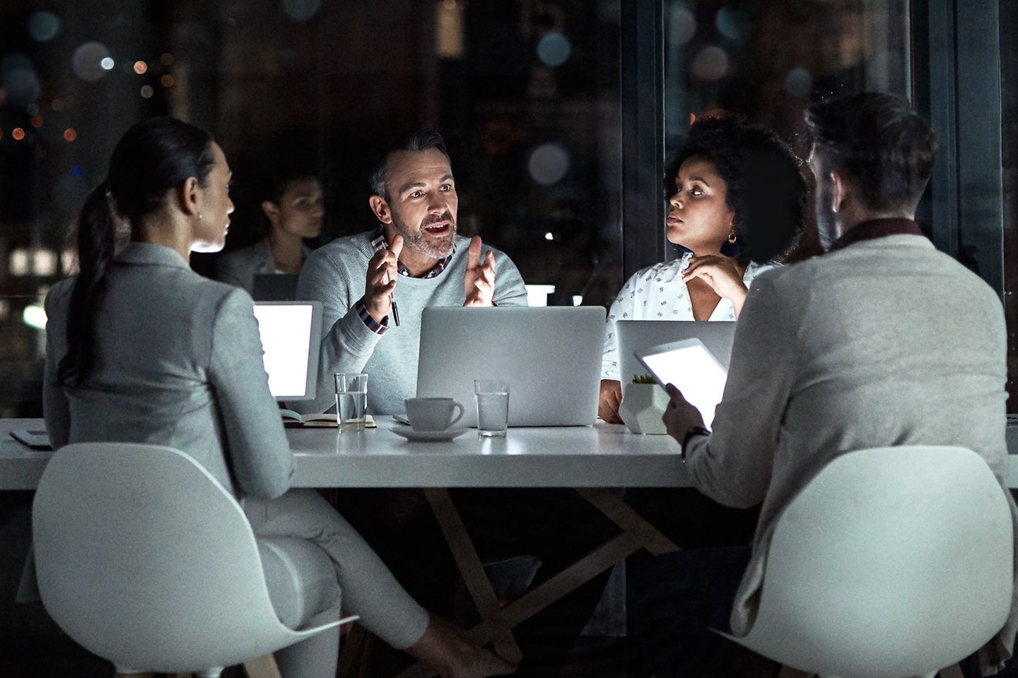 Vier mensen zitten rondom een grijze tafel en zijn in gesprek