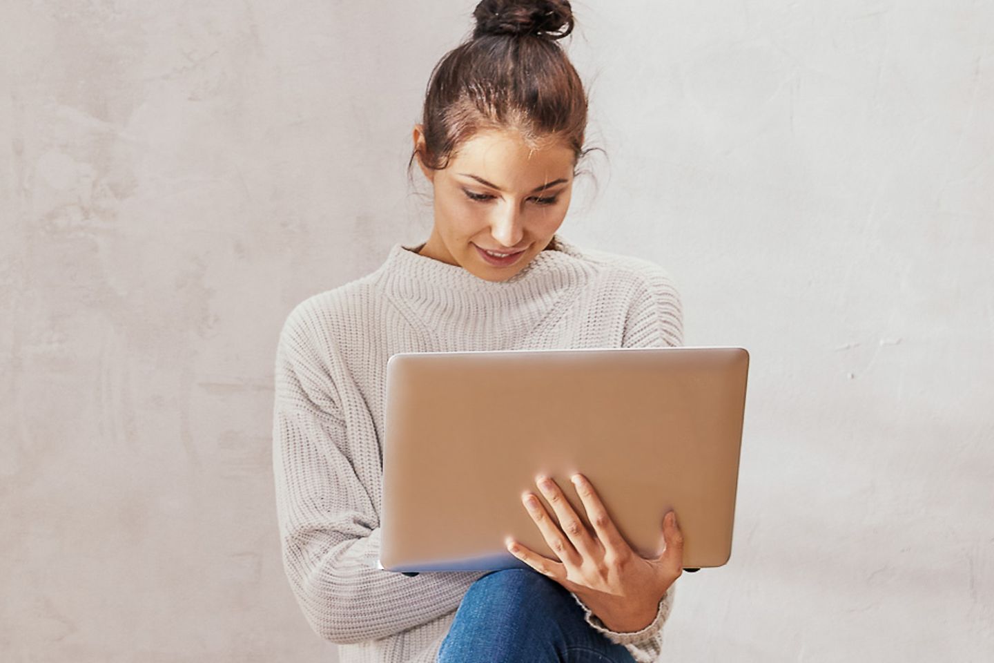 Young woman in front of concrete wall working on laptop