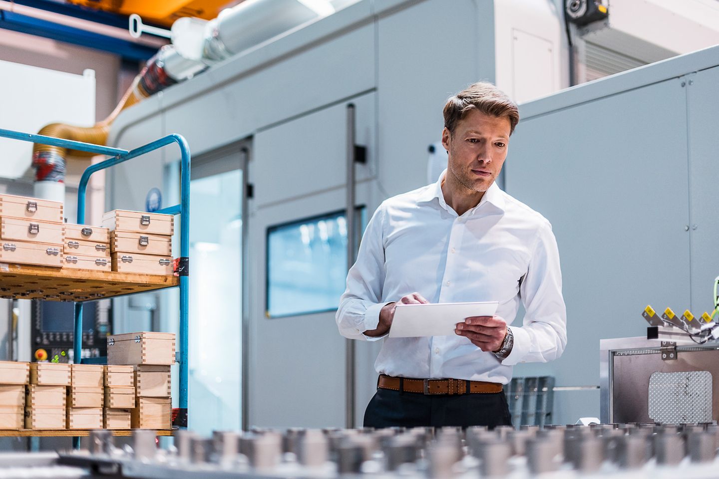 Businessman with tablet in hand stands looking over machine