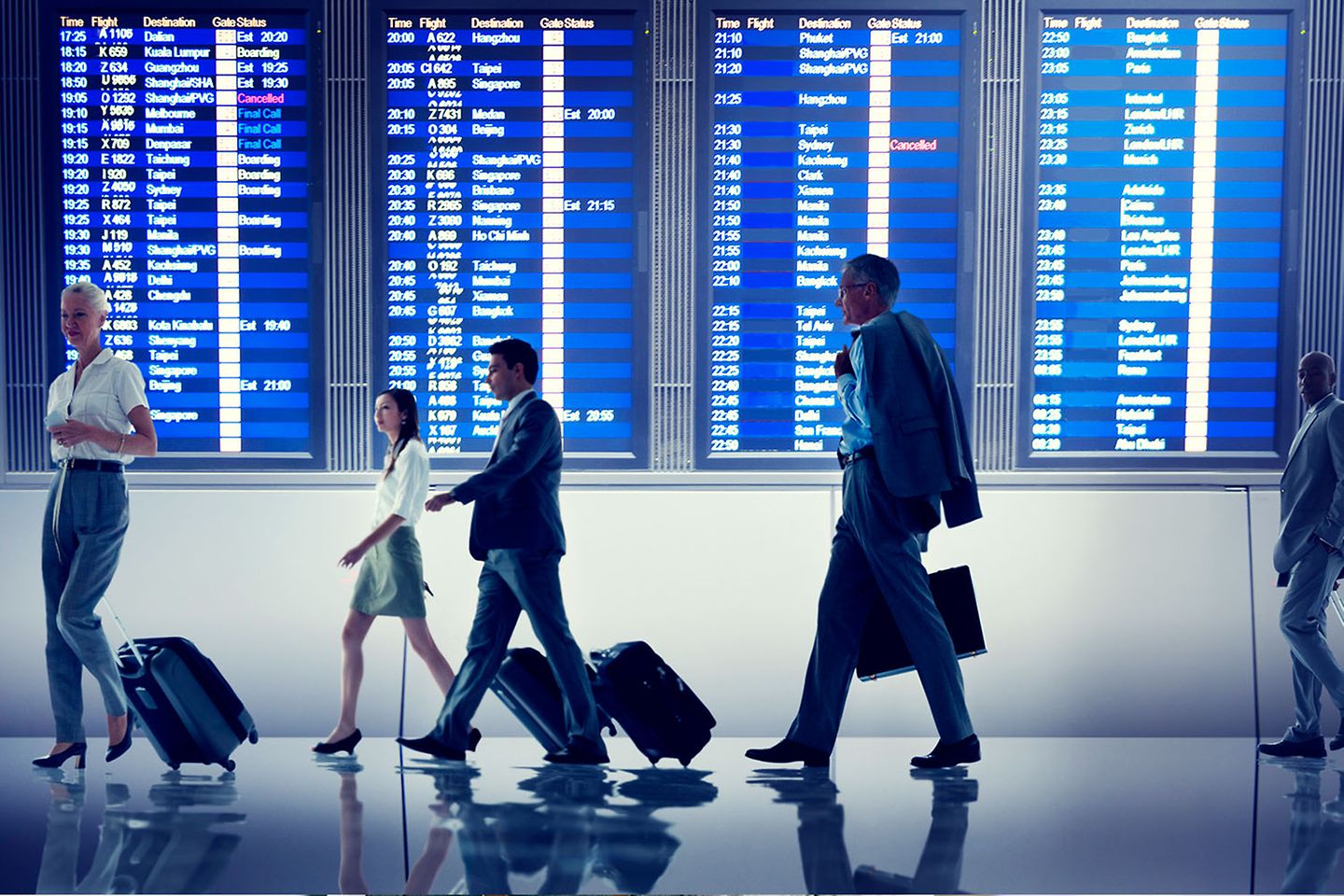 Business people with rolling suitcases in front of a large airport display