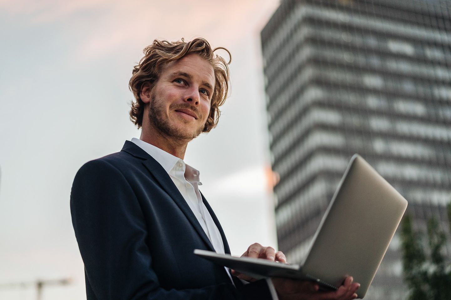 Friendly man standing outside in front of an office building with an open laptop in his handinen offenen Laptop in der Hand