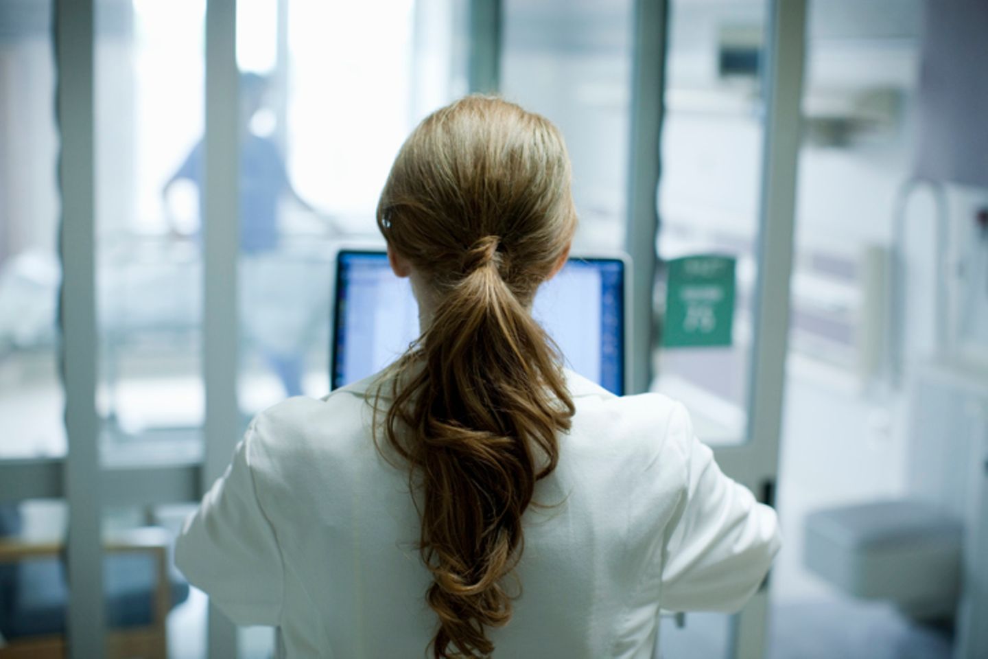 Eine Frau von hinten, die in einem Krankenhaus auf einen Laptop blickt.
