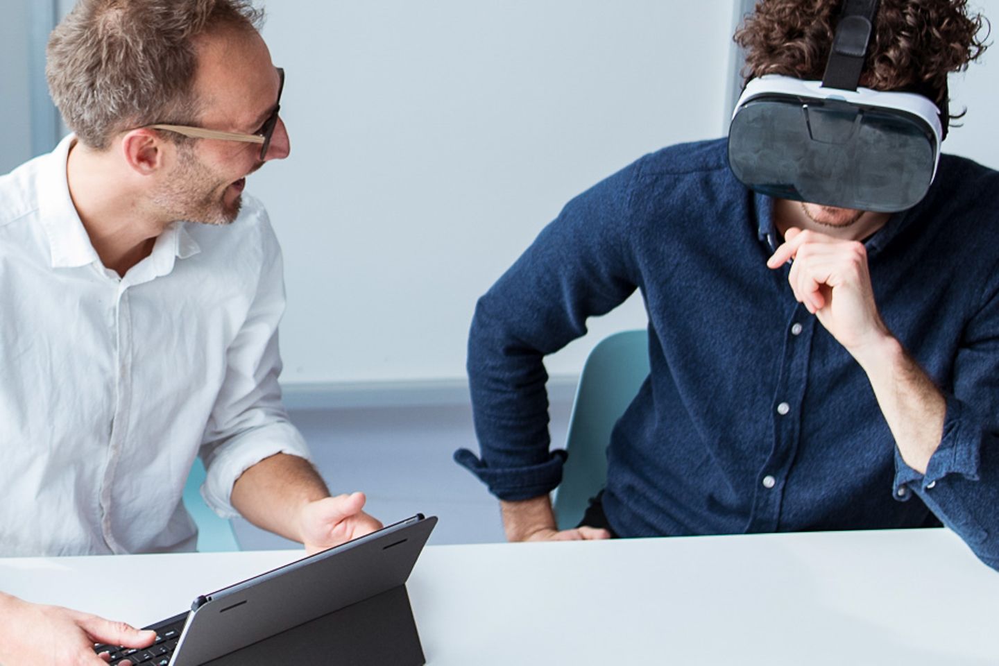 Hombre sonriendo mientras mira a su colega que lleva unas gafas de realidad virtual