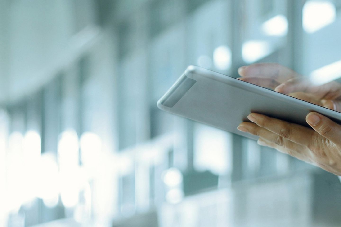 A doctor stands in a hospital hallway typing on a tablet.