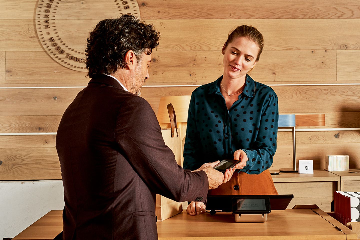 A man shows a woman behind a sales counter something on a smartphone.