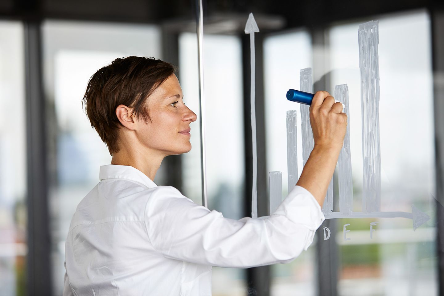 Mujer en la oficina pinta con un marcador diagramas de barras plateados en una pizarra transparente