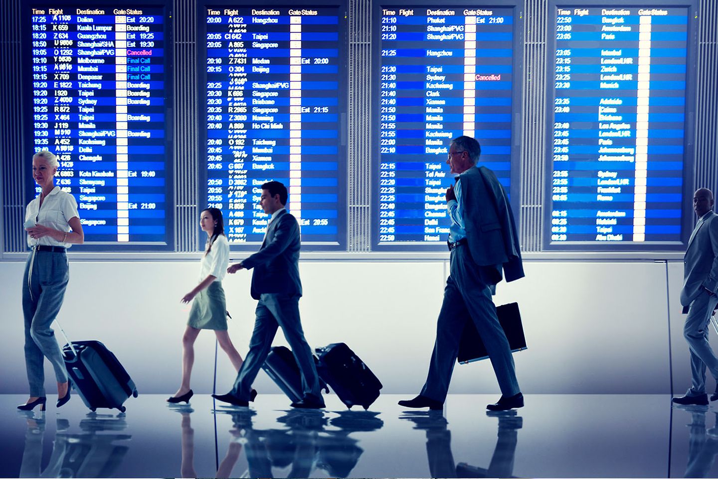 Personas ajetreadas con maletas delante de una pantalla de información sobre los vuelos grande
