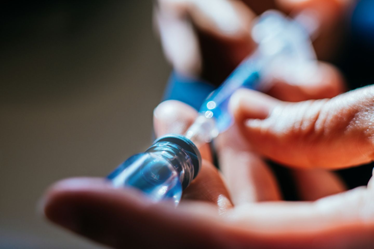Two hands hold a syringe and a medical vial containing a blue fluid
