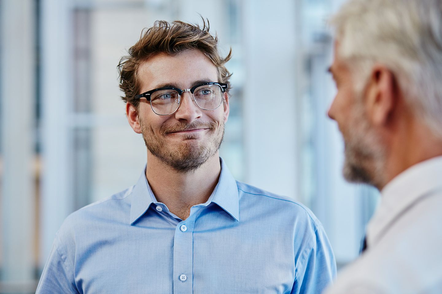 Um jovem empresário de óculos olha sorrindo para outro empresário mais velho