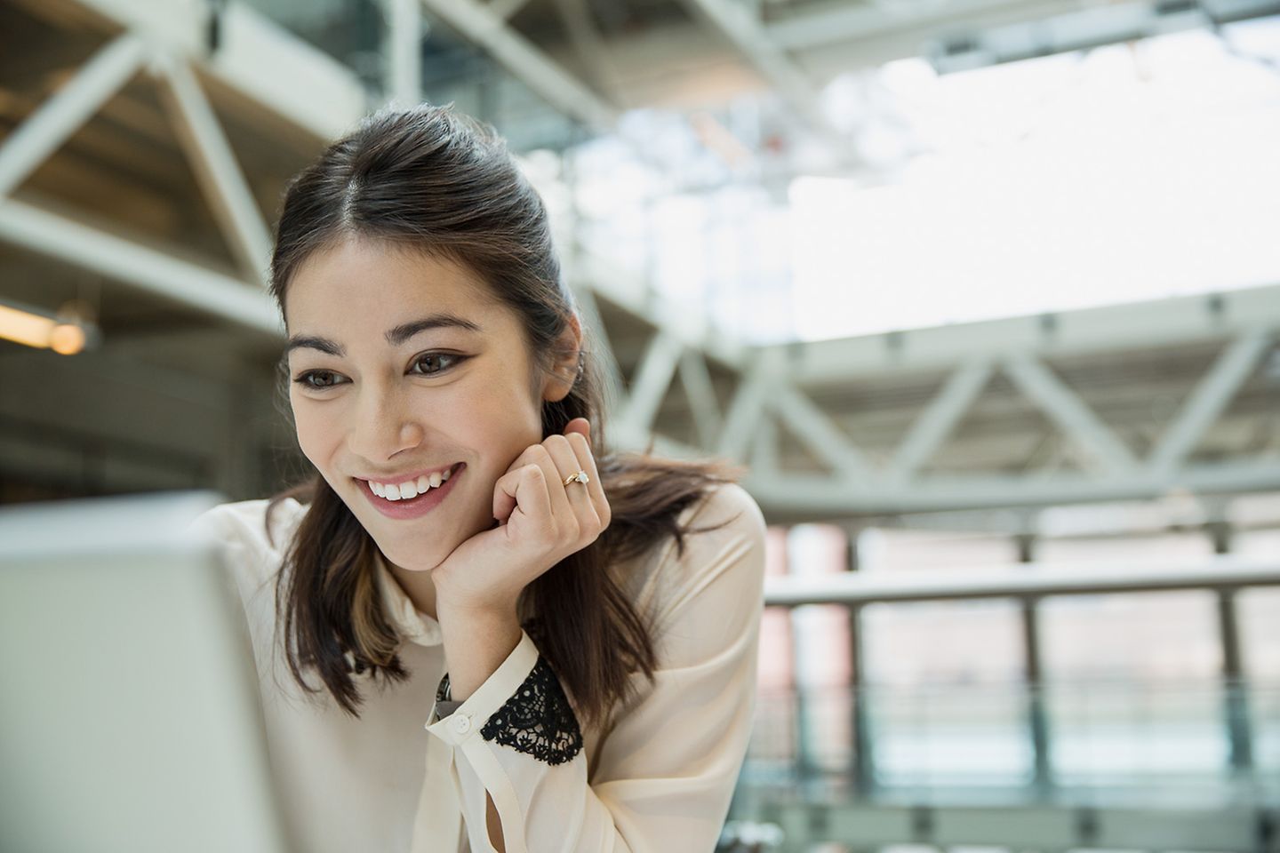 Uma jovem mulher sorrindo olha para a tela do seu laptop