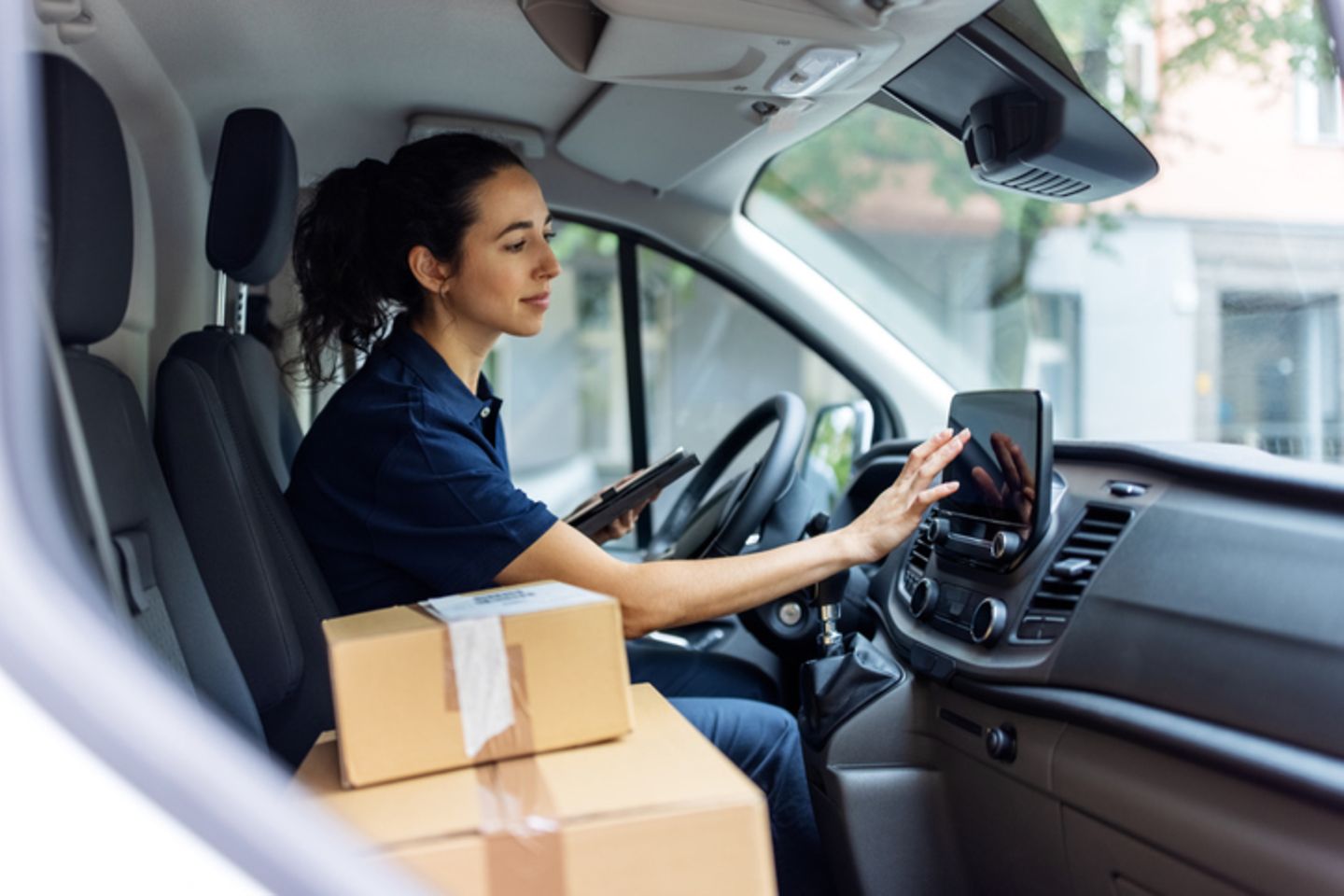 Paketdienstmitarbeiterin im Transporter tippt auf ein Tablet.