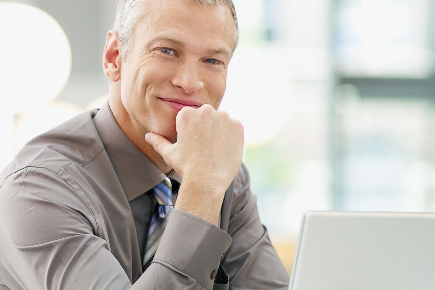 Um empresário está sentado ao laptop sorrindo para a câmera