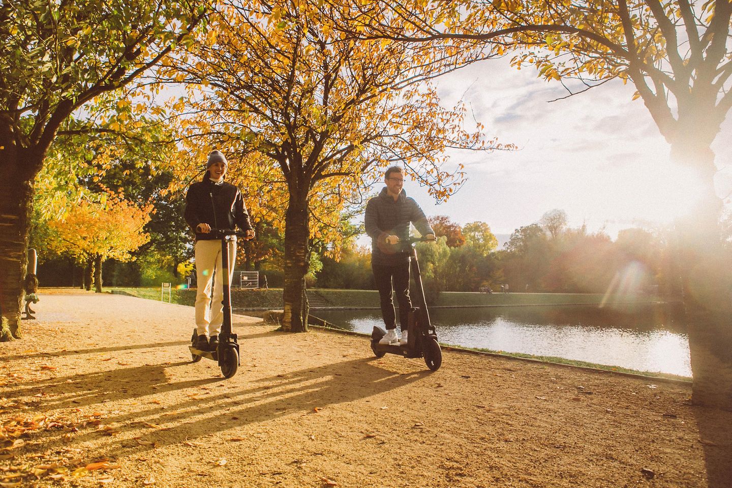 Two men on e-scooters ride in an autumnal park