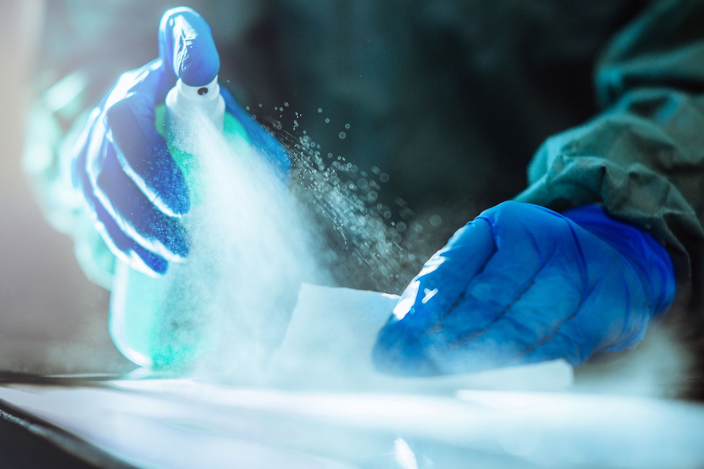 Nahaufnahme zweier Hände in blauen Gummihandschuhen mit Desinfektionsmittel
