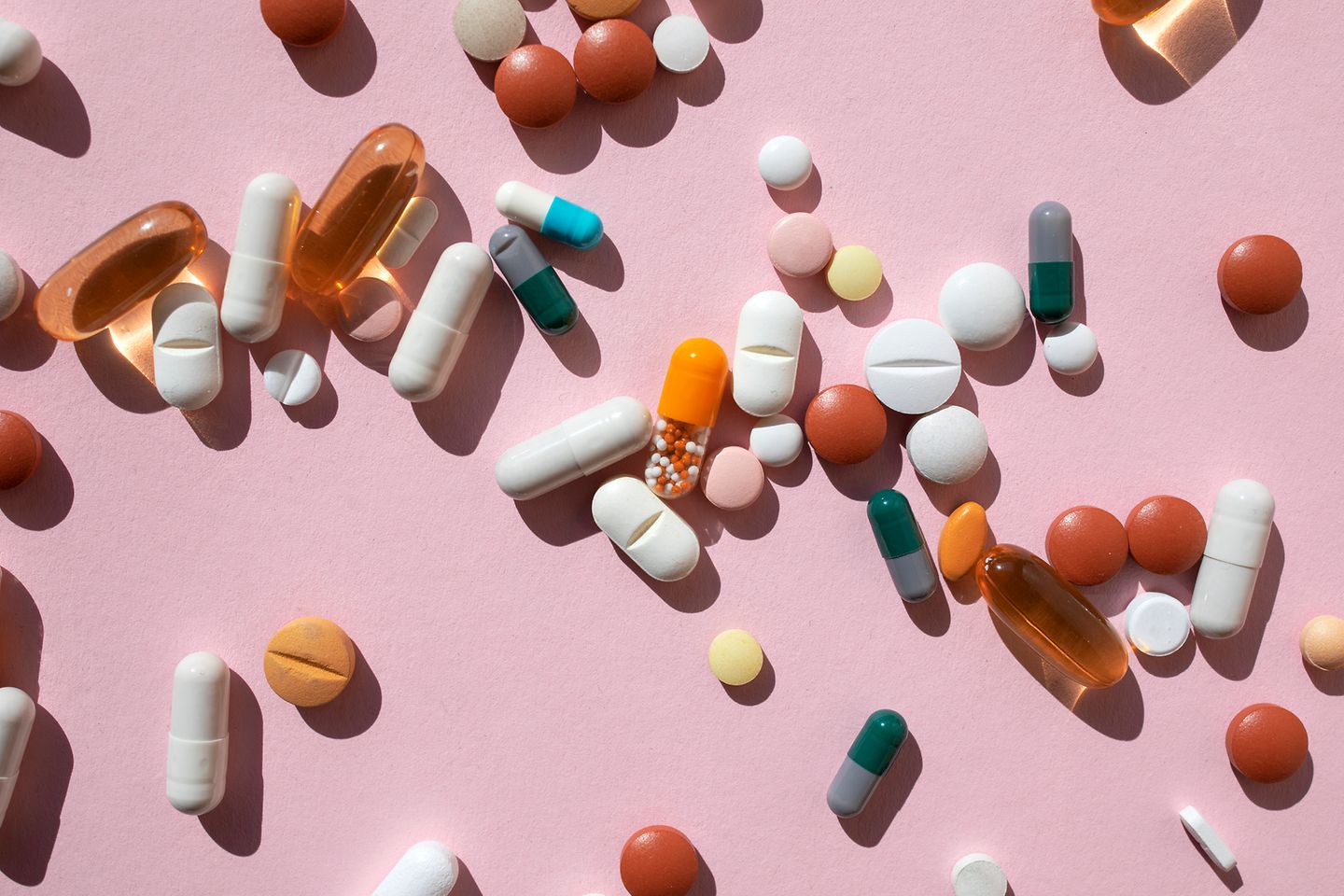 Various tablets and capsules on a pink background