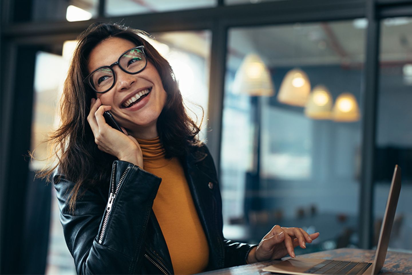 Uma jovem sorrindo senta-se ao laptop e faz uma chamada com o smartphone