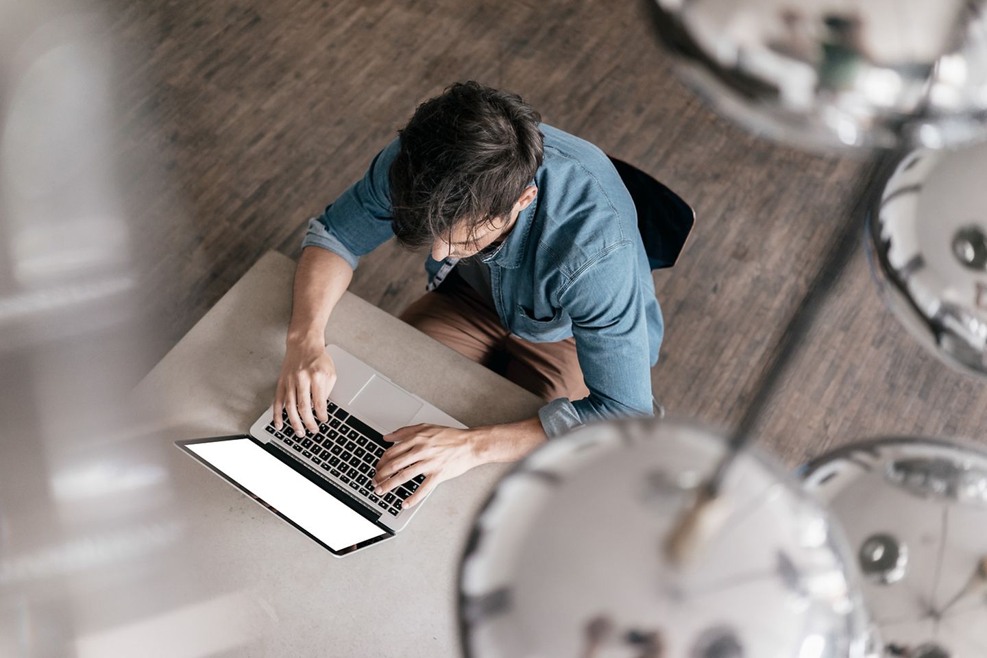 Vista aérea de um homem sentado à mesa. Ele está digitando algo em seu laptop