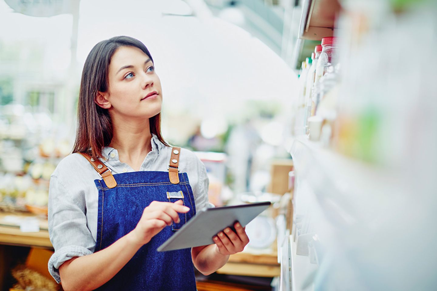 Shop assistant stands in front of supermarket shelf and taps on tablet