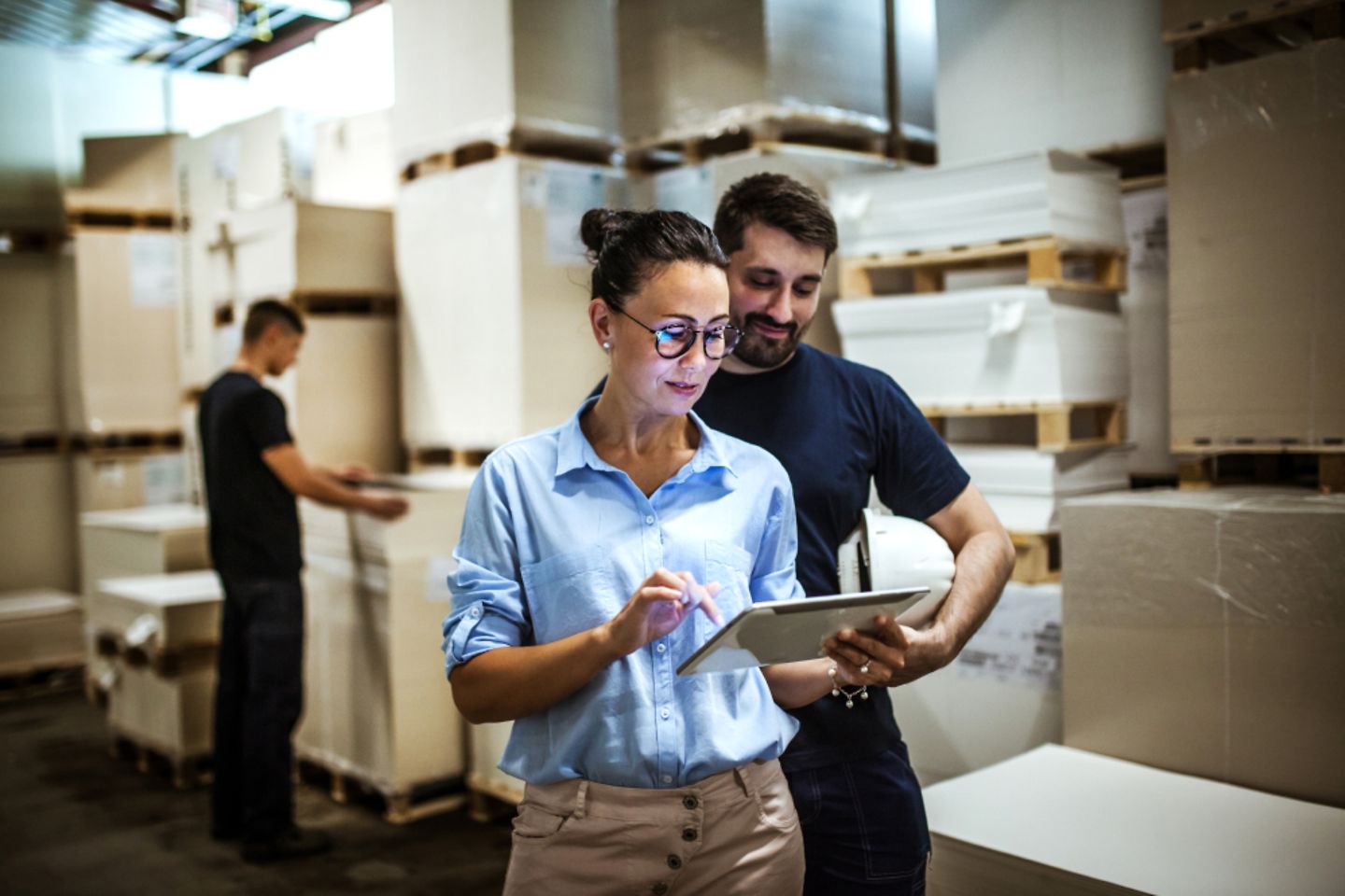 Man and woman looking at a tablet. Pallets and boxes in the background.