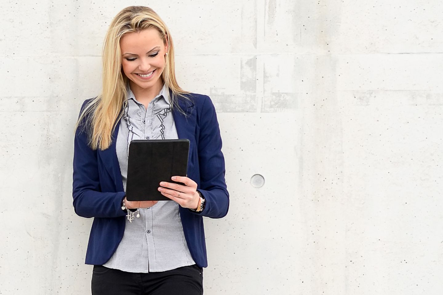 Woman leans on wall and gazes at a tablet smiling. Artistically generated constellation in the form of a padlock.