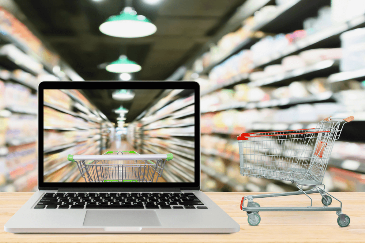 A miniature shopping trolley stands next to a laptop with supermarket shelves in the background.