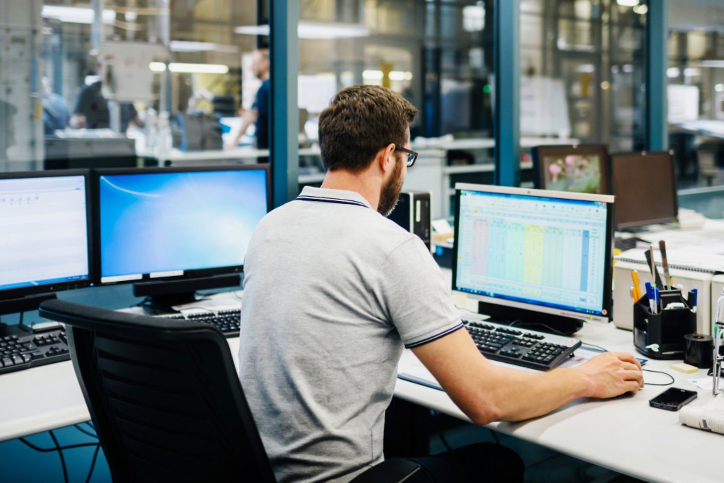 A man in a gray polo shirt sits in front of two computer screens