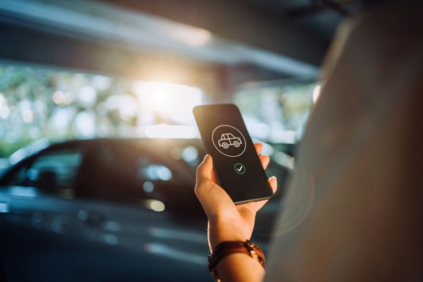 A hand holding a cell phone with a car sharing symbol, with a car in the background 