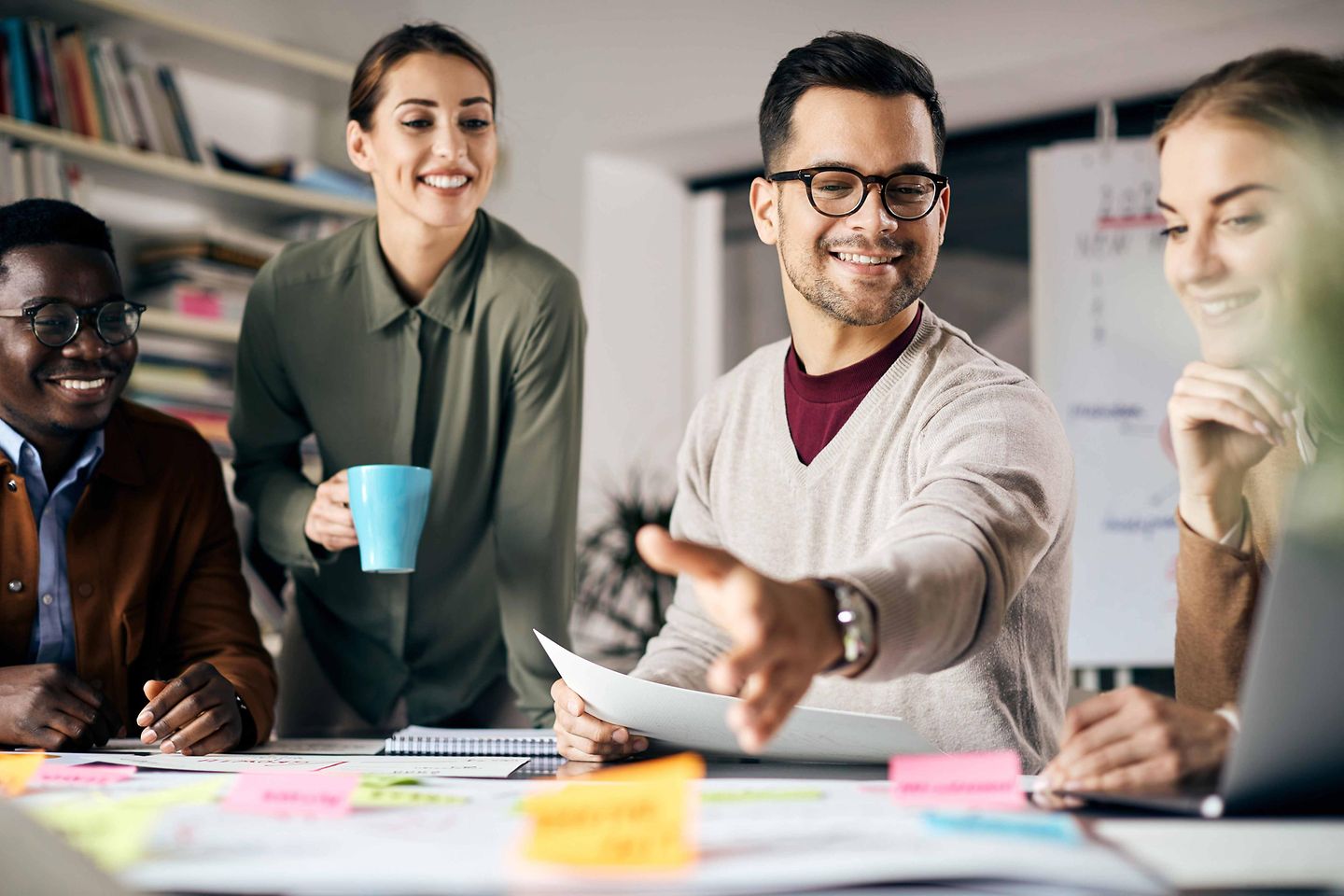  Mehrere Personen stehen und sitzen an einem Tisch und arbeiten zusammen