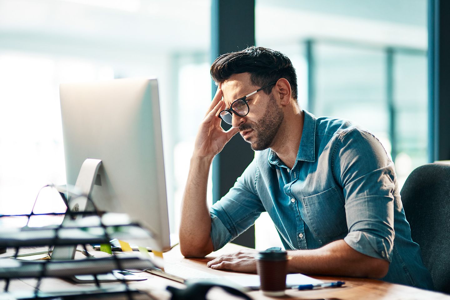 Hombre con gafas sentado en la mesa de trabajo mirando al monitor pensativo o leyendo algo