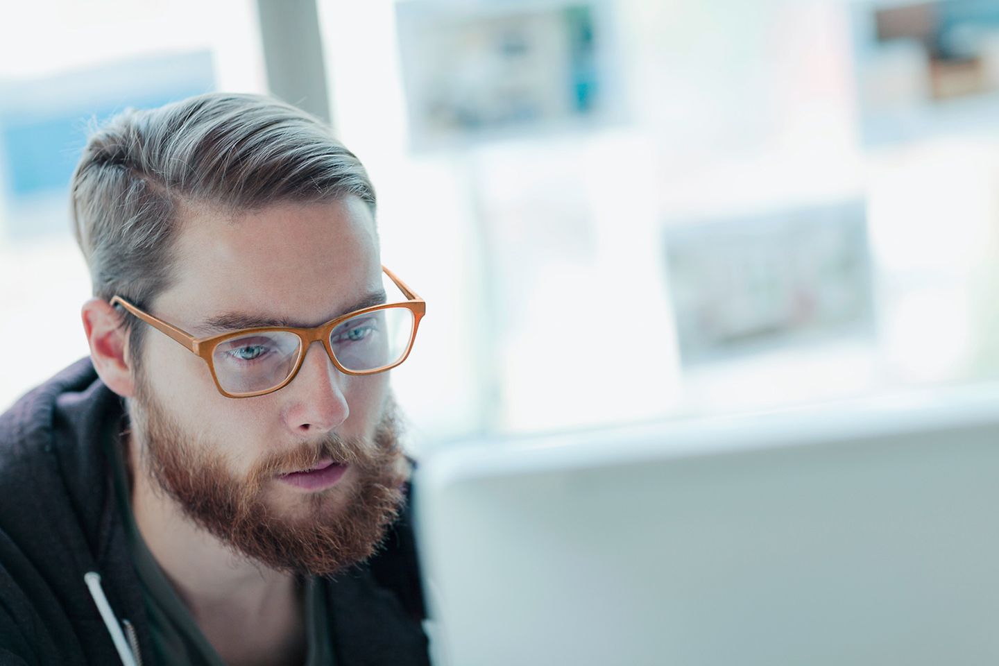 Hombre joven con gafas rojas y barba mirando concentrado al monitor