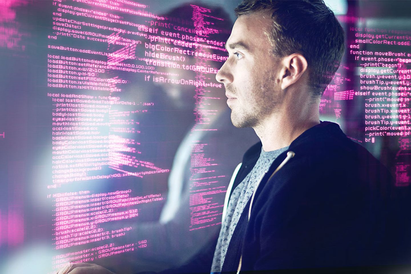 A man sitting infront of a screen with coding everywhere in magenta 