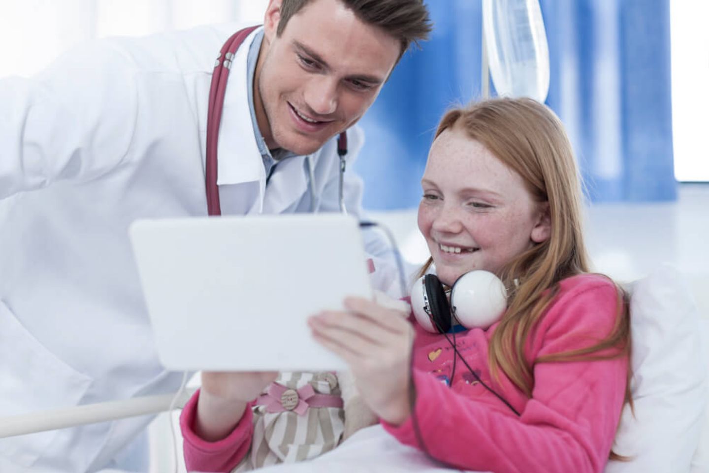 Arzt und Maedchen schauen auf Tablet in einem Krankenhauszimmer