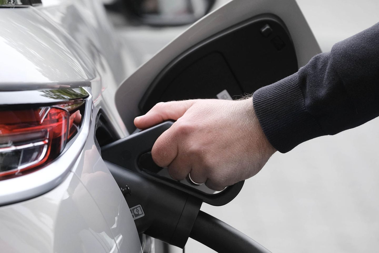 A hand holds a charging cable that is plugged into a car