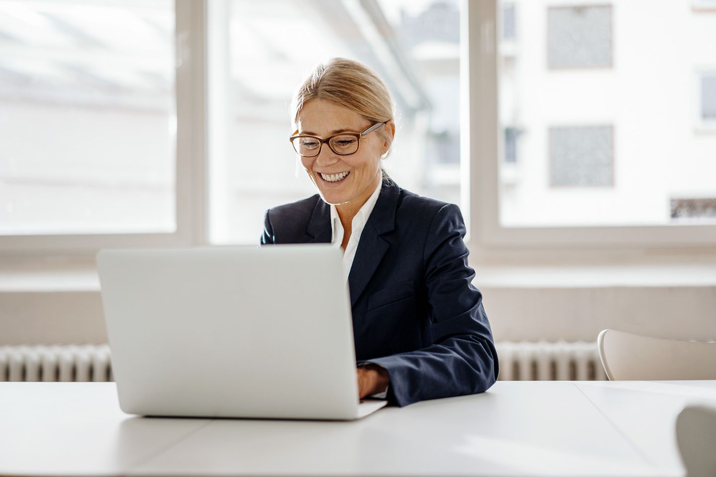 Lachende zakenvrouw zit aan bureau en werkt op laptop