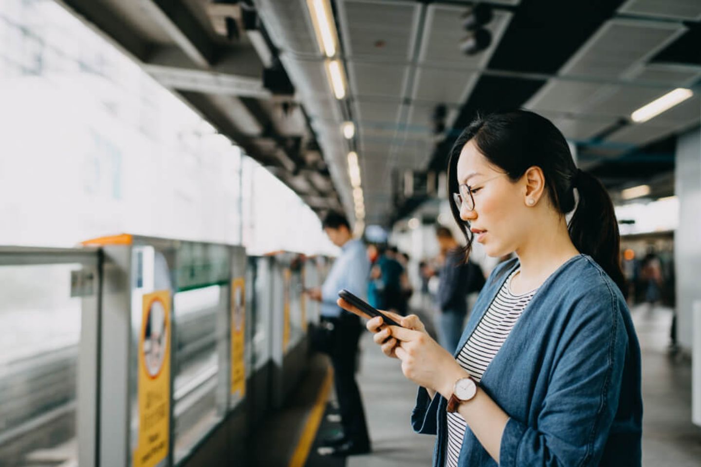 Frau benutzt Smartphone auf dem Bahnsteig einer U-Bahn-Station
